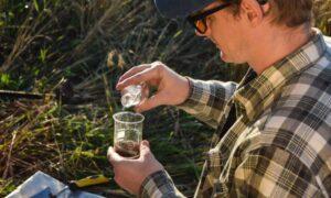 Technician performing a perc test by pouring water into a soil sample in Denver