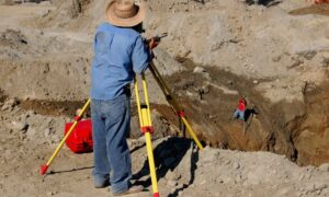 Surveyor using a total station for a construction staking survey on an undeveloped site with workers marking ground locations