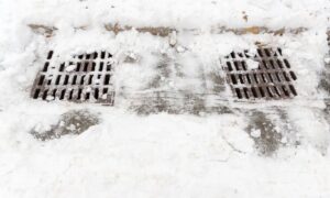 Snow-covered drainage grates on a paved surface, illustrating the drainage features that construction staking helps position accurately