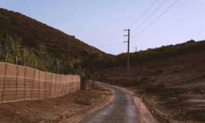 Narrow private access road winding through steep terrain with utility poles and wooded hillsides