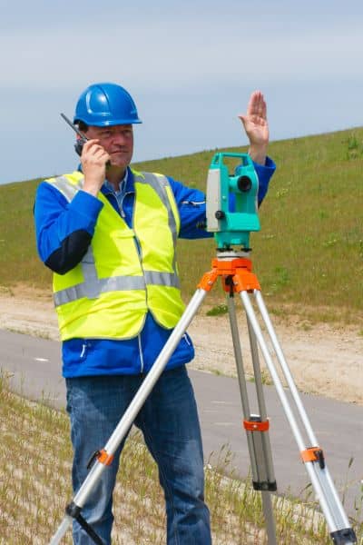 Property line surveyor fieldwork - ALTA SURVEY Colorado Licensed land surveyor using a total station to mark property lines near a roadway during a property line survey
