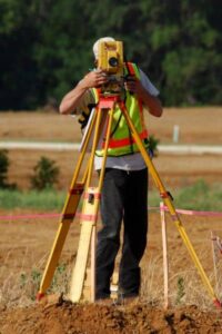 Licensed land surveyor using theodolite for accurate boundary survey in an open field