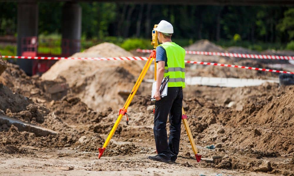 Land surveyor using total station on muddy ground after flood to update an ALTA Land Title Survey
