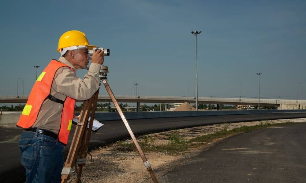 Alta surveys highway construction - ALTA SURVEY Colorado Land surveyor using tripod equipment beside a highway construction site, demonstrating how alta surveys support accurate planning and major development projects