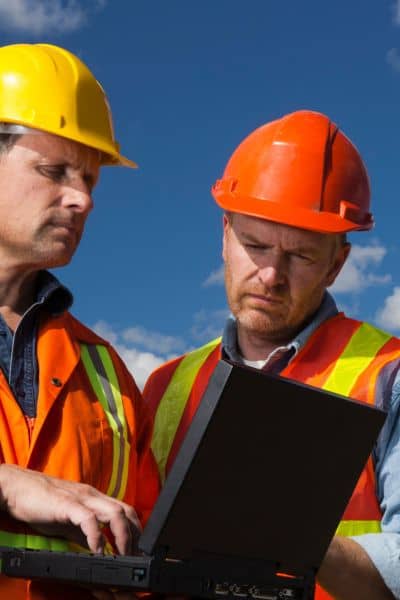 Engineers reviewing flood and mapping data on a laptop for an ALTA Land Title Survey after heavy storm damage