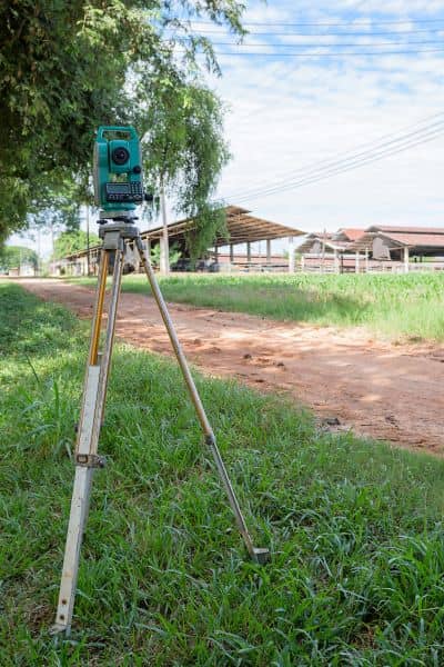 A surveyor’s total station set up in the field, used to collect elevation data for a topographic survey after drainage changes