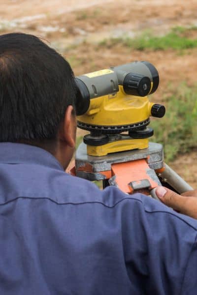 Surveyor using a level to measure ground slope on a construction site